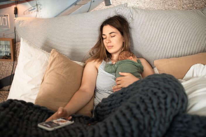 A woman resting on the bed with her baby on top