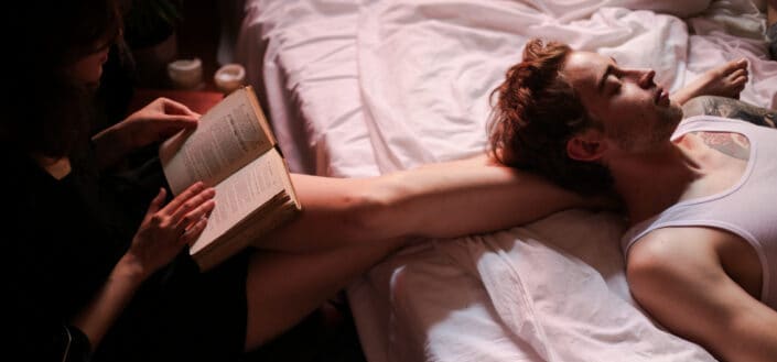 Man lying resting on a girl's legs while she is reading a book
