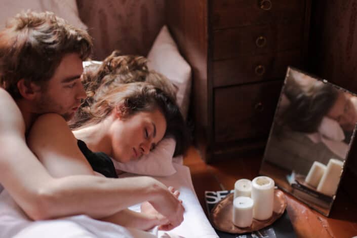 Woman in Black Tank Top Lying on Bed With a Man Hugging Her