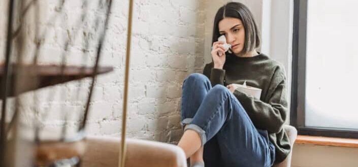 Desperate young ethnic female millennial crying on couch and wiping tears