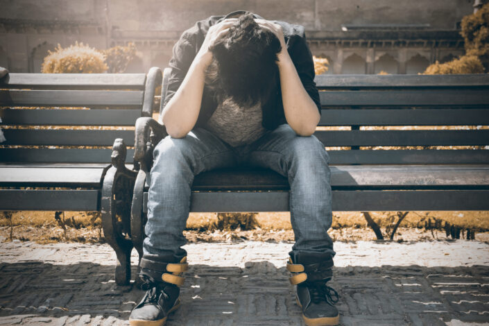 Man in black shirt and gray denim pants sitting on gray padded bench