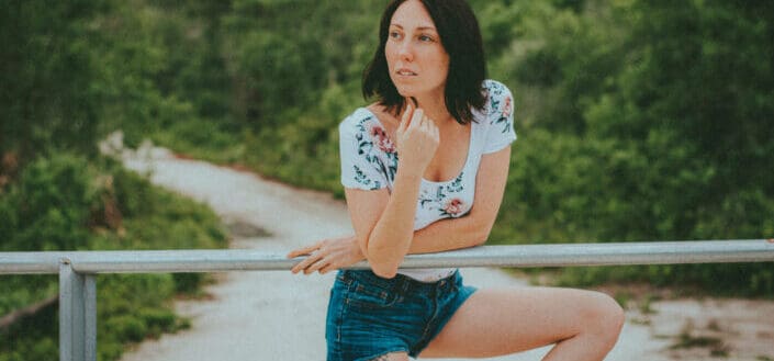 A woman in floral shirt and blue denim shorts standing beside metal railing
