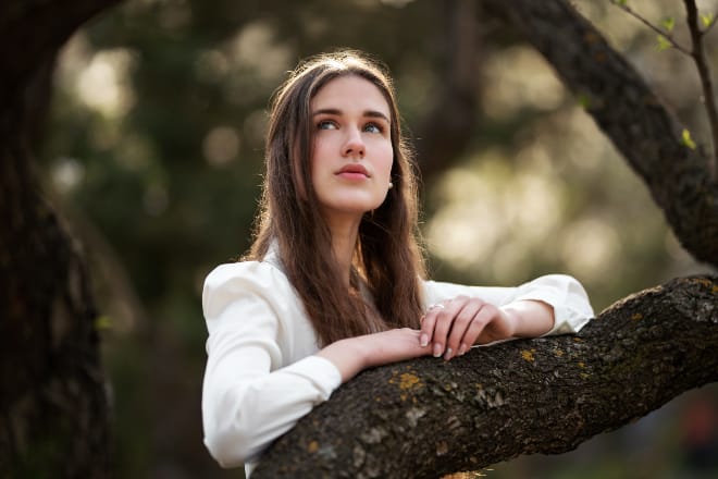 Woman in White Long Sleeve Shirt Leaning on Tree Trunk - What Makes a Beautiful Woman