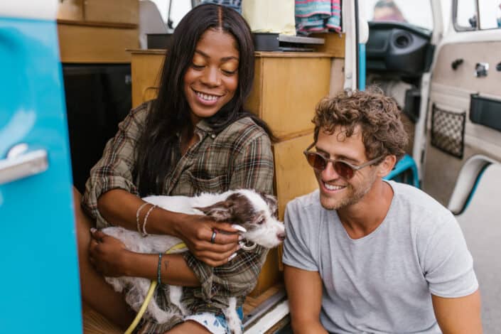 Couple sitting outside their camping truck playing with their dog