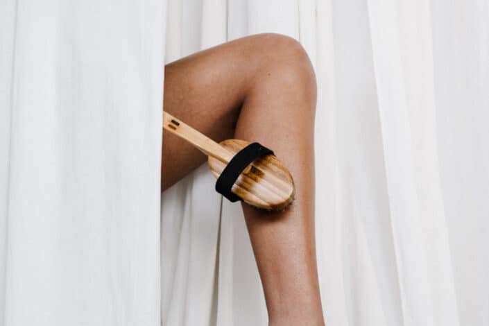 A woman scrubbing her legs with a wooden body scrub