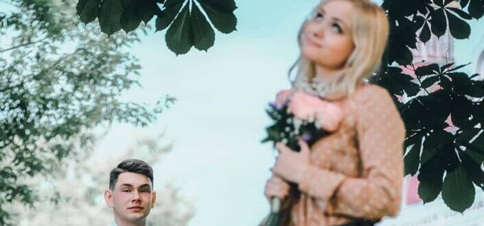Woman with bouquet standing in park near boyfriend