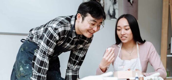 A man in plaid shirt wearing eyeglasses talking to the woman sitting near the table
