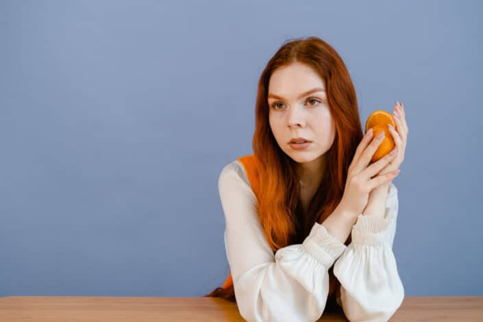 A woman in white long sleeves holding an orange fruit