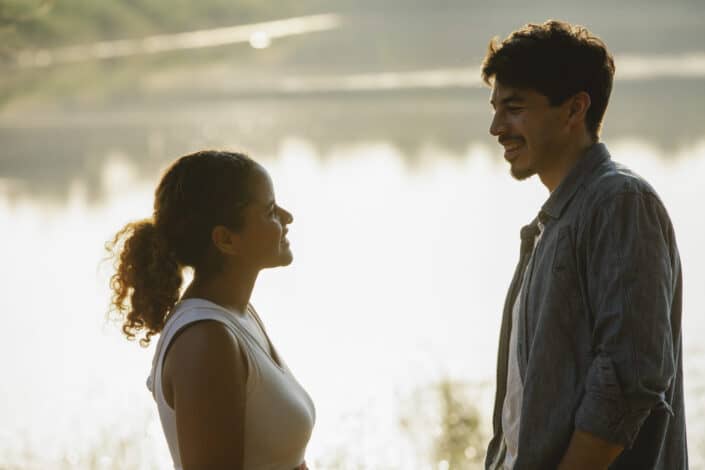Cheerful loving diverse couple smiling at lakeside at sundown