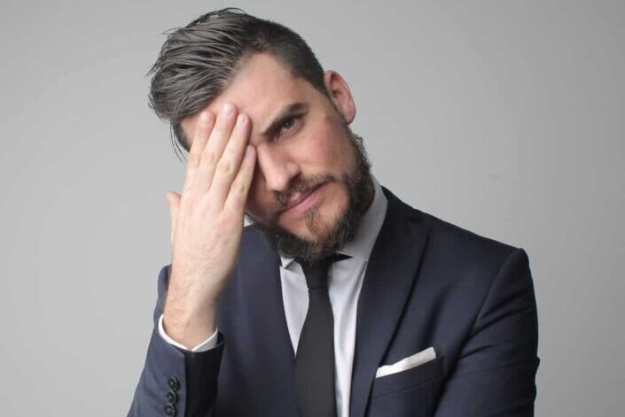 Man in black suit jacket touching his face