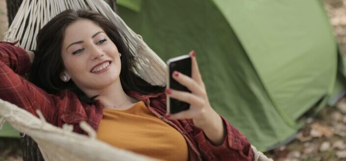 woman lying on hammock while using cellphone