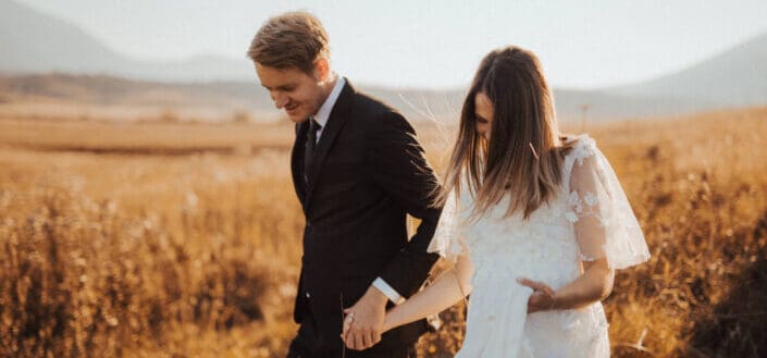 man in black formal suit holding womans hand in white dress