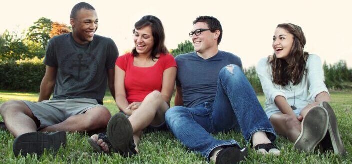 Smiling women and men sitting on green grass