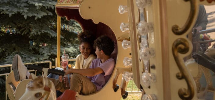 Teenage couple sitting in carousel seat smiling and talking to each other