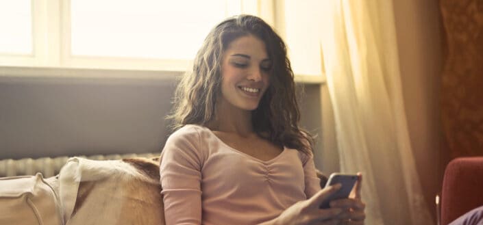 Woman reclining on bed while using a smartphone