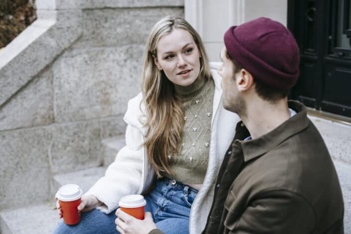 Young couple talking and drinking beverages on stairs