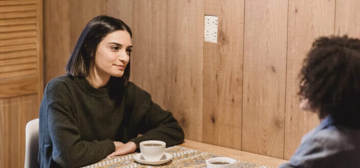 Best friends speaking at table with cups of coffee