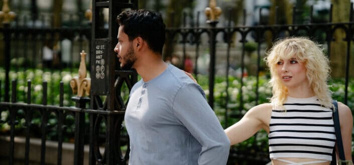 Brunette man and a blond woman standing by a black metal fence in a city