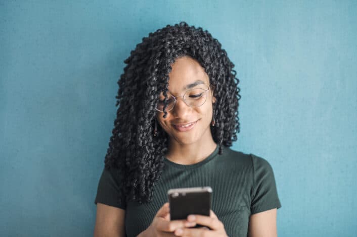 smiling woman in black t shirt and glasses using her smartphone