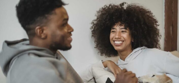 Positive black couple resting in bed with dog and chatting
