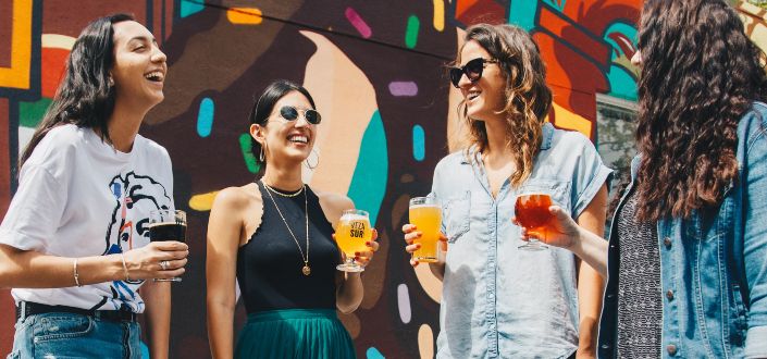 four women holding drinks while laughing together