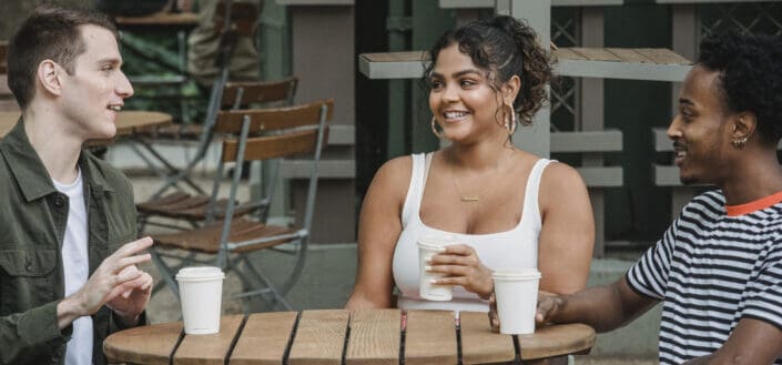 Smiling young teenagers drinking coffee and chatting in street cafe