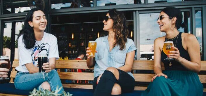 Three Women Sitting on a Bench While Drinking