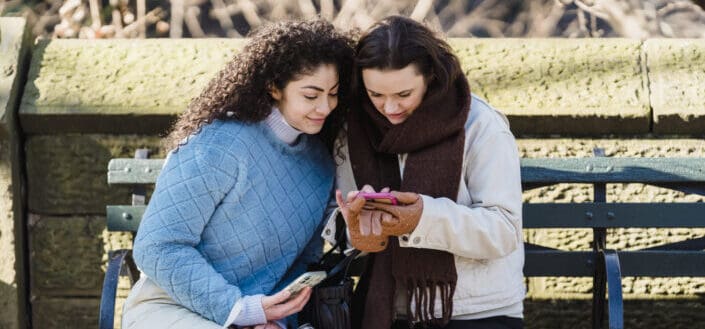 Women using smartphone together on bench in park