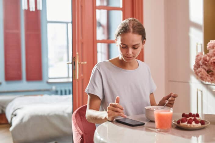 Woman eating her breakfast while using her smartphone