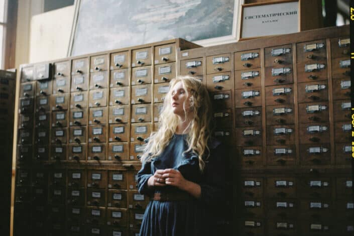 Woman in blue long sleeve dress standing beside brown wooden cabinet