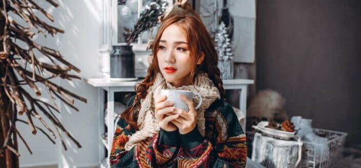 woman in brown and white tribal coat holding white ceramic mug