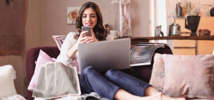 Smiling woman using smartphone while lying on couch