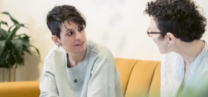 Young female colleagues discussing project sitting on couch during remote work