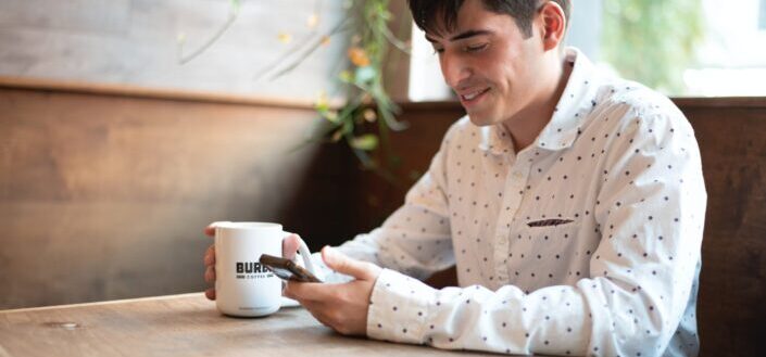 man using phone with mug in hand