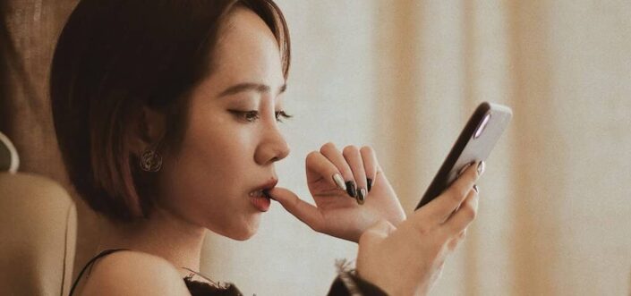 Woman Using Smartphone While Biting Her Nail