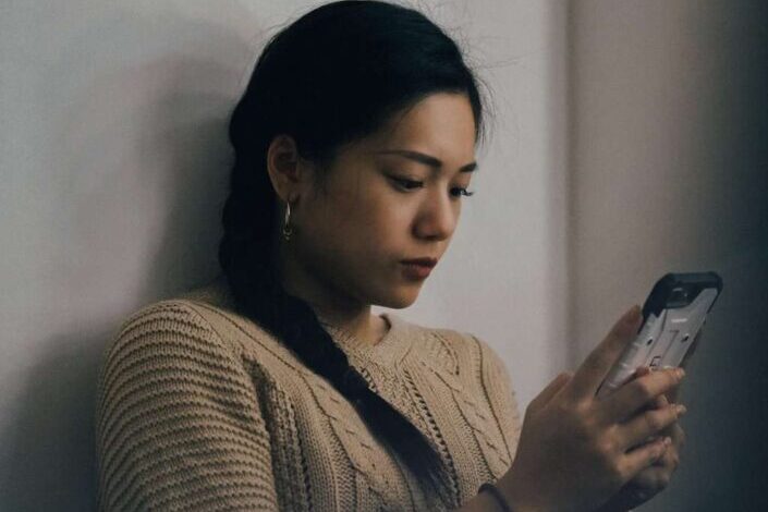 Woman Leaning on White Wall Using Smartphone