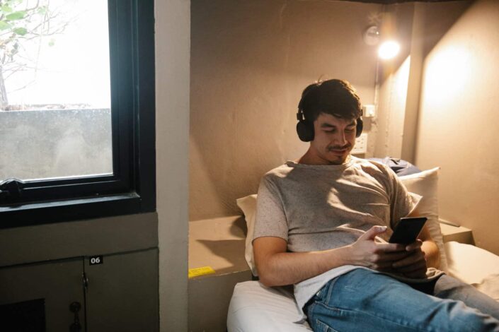 Smiling man resting on bed using smartphone