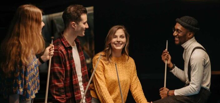Happy Friends Holding Cue Sticks at a Pool Table