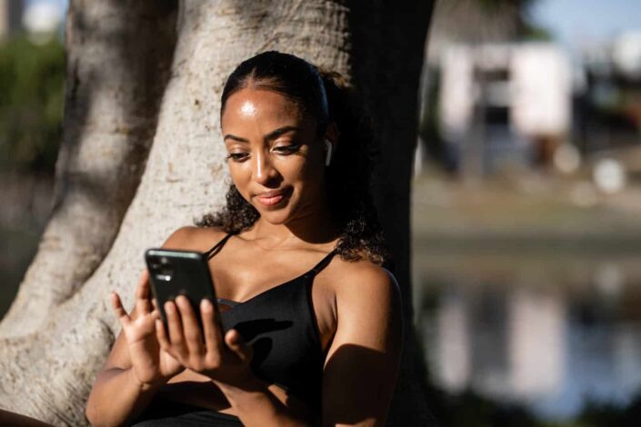 Woman holding cellphone while leaning on tree
