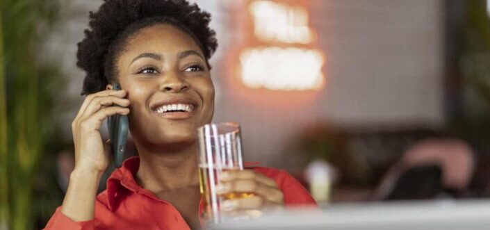 Woman in Red Smiling and Talking on Phone While Drinking