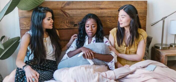 Women sitting on bed comforting a sad woman