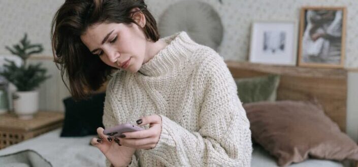 Woman Sitting on Bed While Using a Smartphone