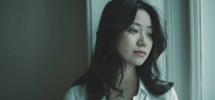 young female looking out window pensively