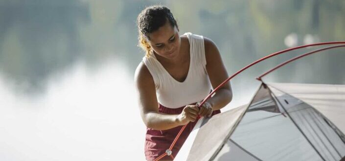 Focused traveler putting up tent near pond