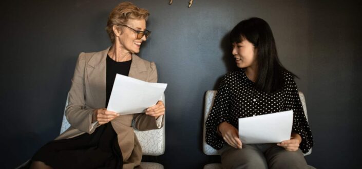 two women holding documents while seated