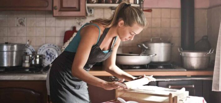 Young woman rolling dough in kitchen