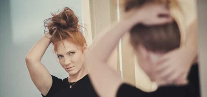 woman looking at a mirror holding her hair