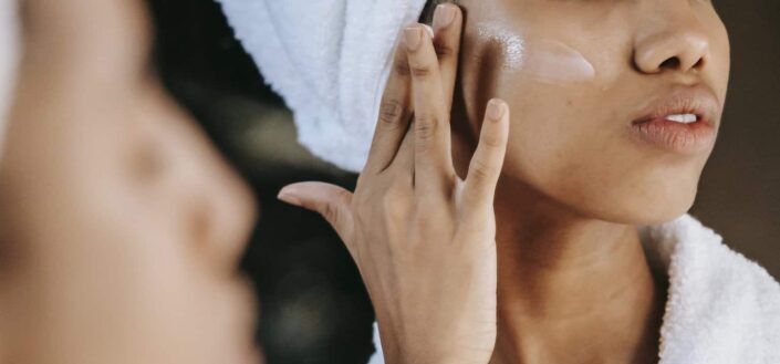 woman applying cream on face against mirror