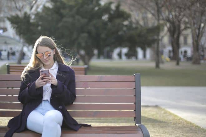 woman sitting on bench using her phone - How Often Should A Guy Text You In The Beginning