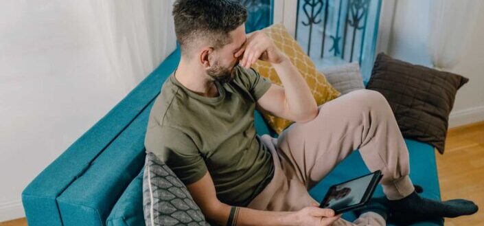 man crying while sitting on a blue sofa